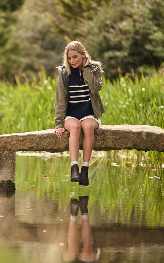 Woman sitting on a log over water with greenery in the background