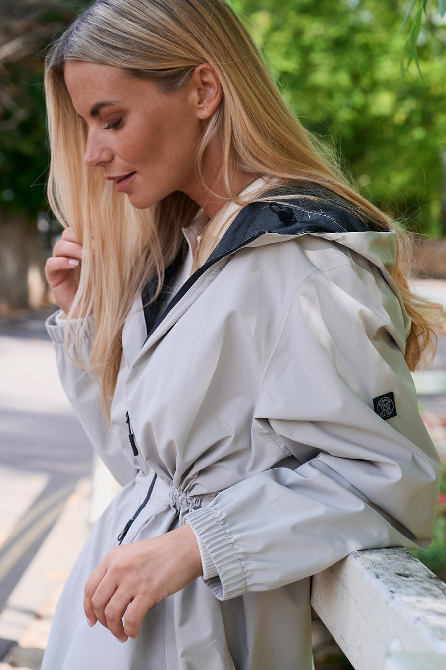 Woman wearing a light-colored Dubarry raincoat with a blurred green outdoor background